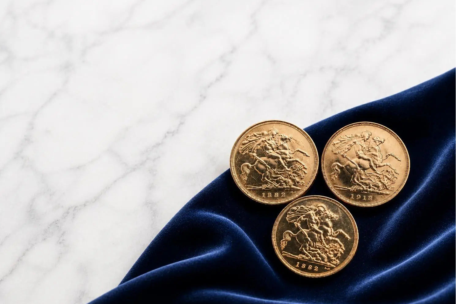 Three gold sovereign coins on a blue fabric with a white marble textured background | 888 Bullion